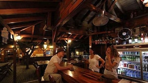 Un bar rústico con vigas de madera, barra y mostrador refrigerado.