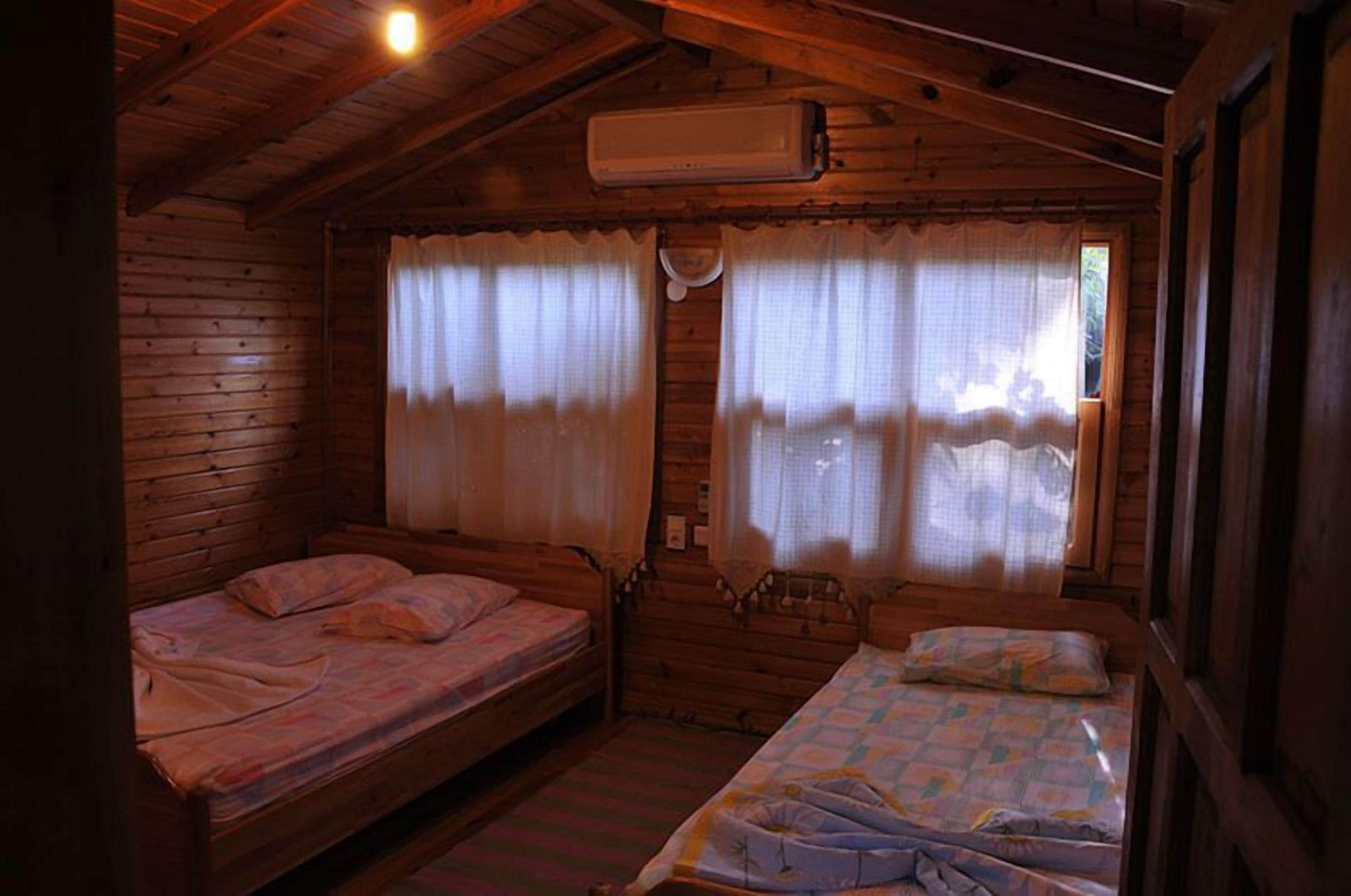 Una cabaña pequeña con dos camas de madera, un ventilador de techo y una ventana con cortinas.