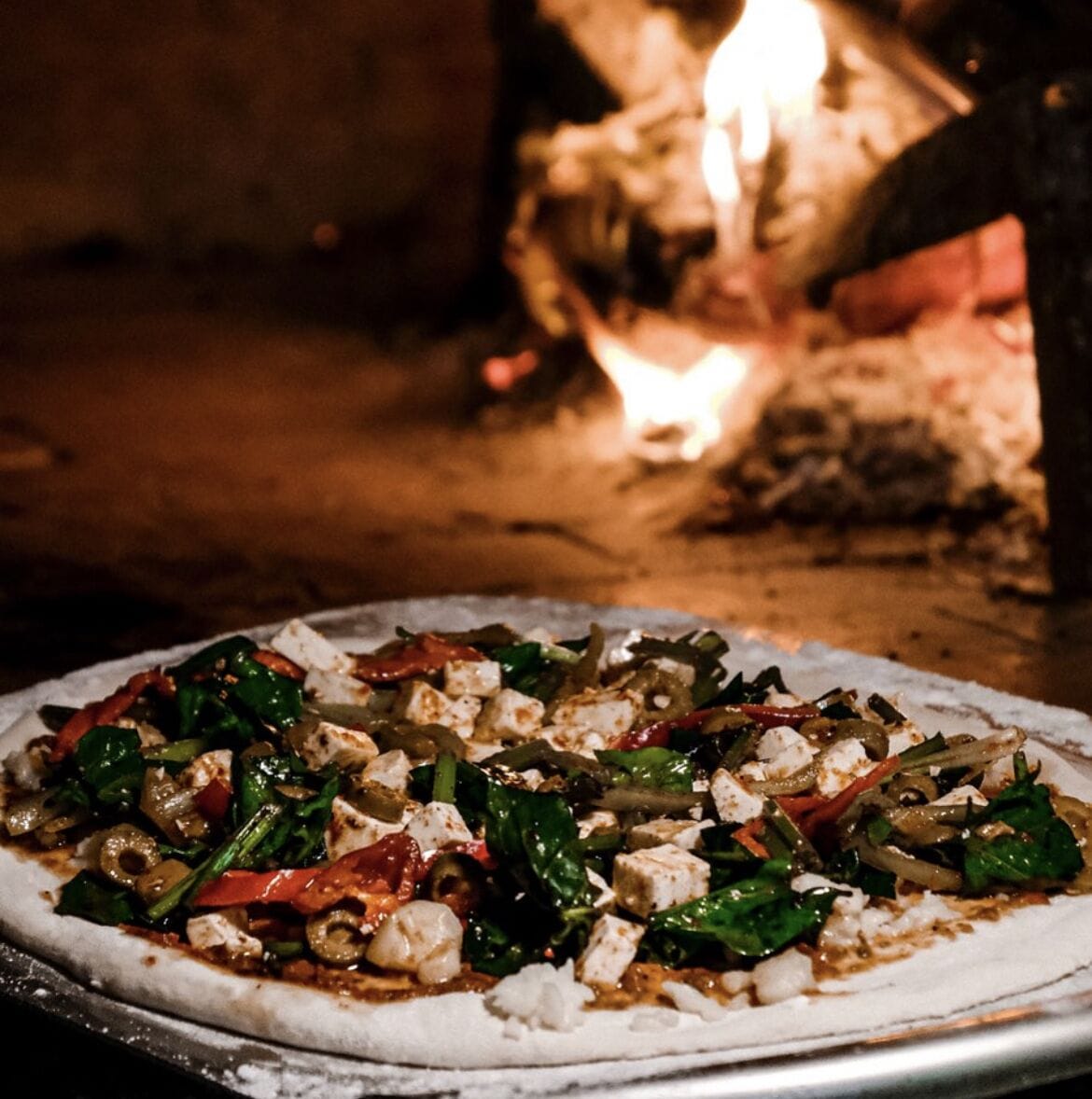 A pizza with various toppings in front of a wood-fired oven.