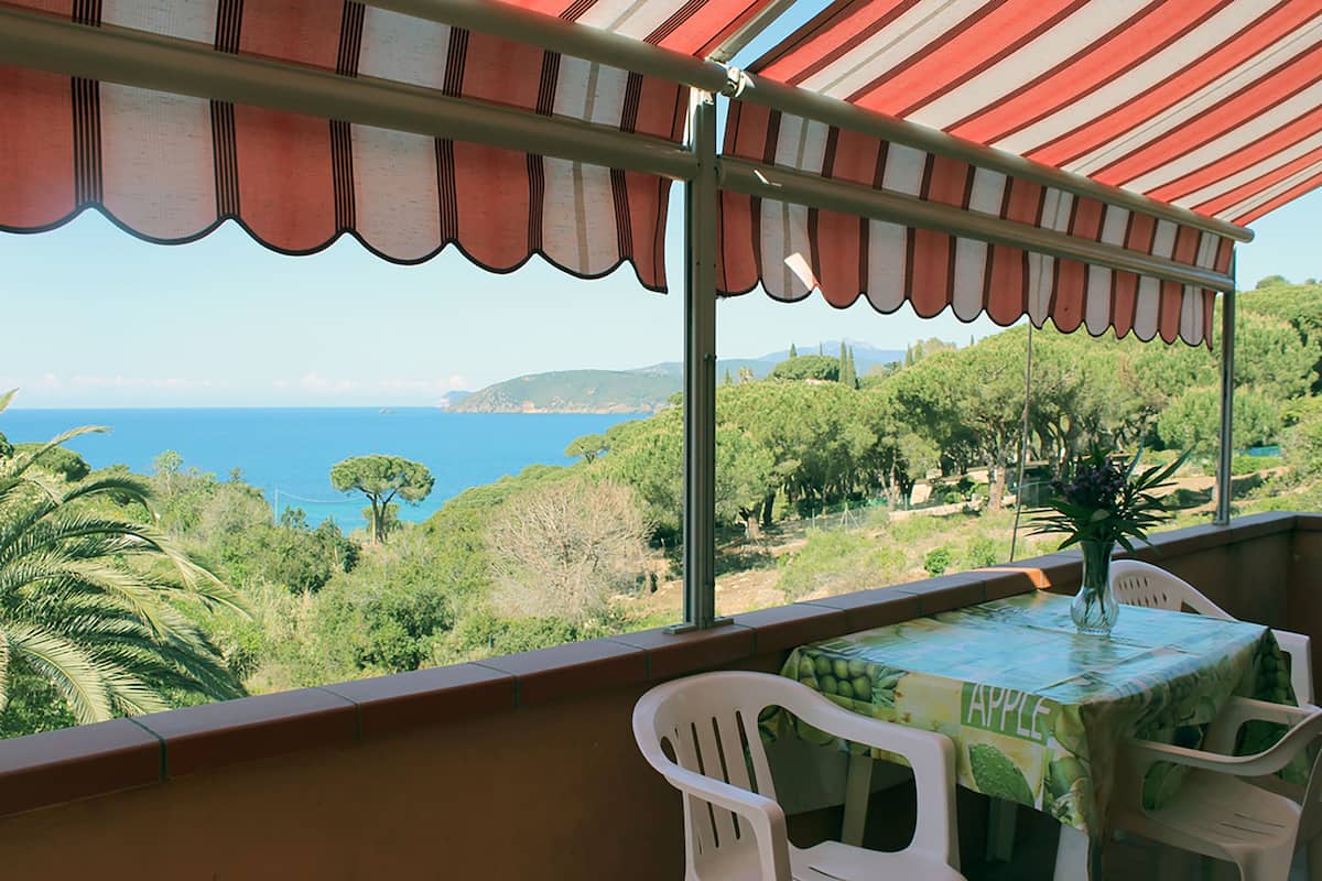 A balcony with a table and chairs, overlooking a scenic view of the sea and greenery.