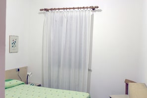 A bedroom with a bed, a bedside table, a lamp, a chair, and a curtain. - Casa Roberta (Capoliveri)