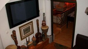 Habitación con televisión de pantalla plana en la pared, escalera de madera que conduce a un comedor y diversos objetos decorativos, incluyendo una guitarra y cerámica.