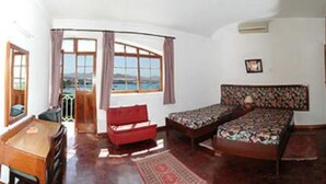 Habitación con dos camas, un escritorio y una silla. Amplias ventanas con cortinas y vista al mar.
