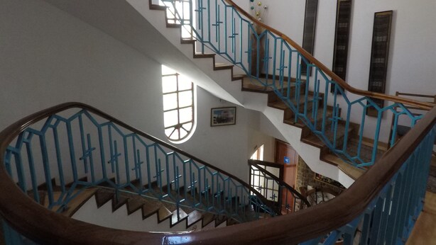 Un interior de varios niveles con una escalera de madera y barandillas azules.