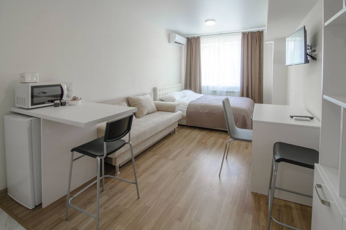 Quarto de hotel compacto com cozinha compacta, uma cama, escrivaninha e uma cadeira.