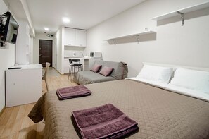 Ein kleines Hotelzimmer mit Bett, Schreibtisch, Stuhl und einer Küchenzeile.