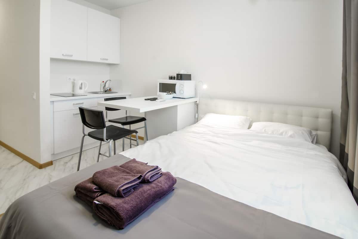 Quarto de hotel com cama, escrivaninha com cadeira, micro-ondas e chaleira.