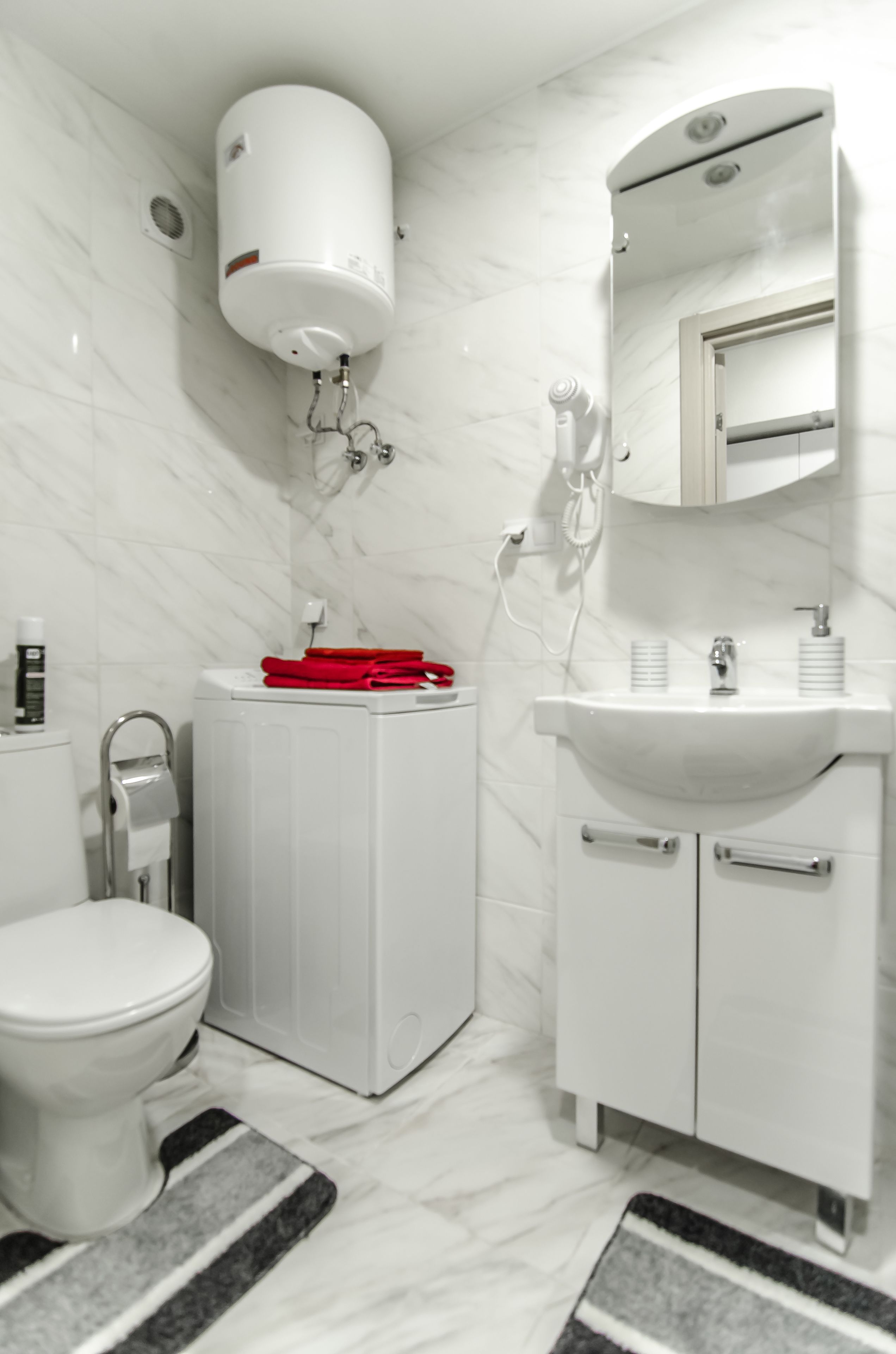 Ein modernes Badezimmer mit Toilette, Waschmaschine und Waschbecken mit Spiegel darüber.