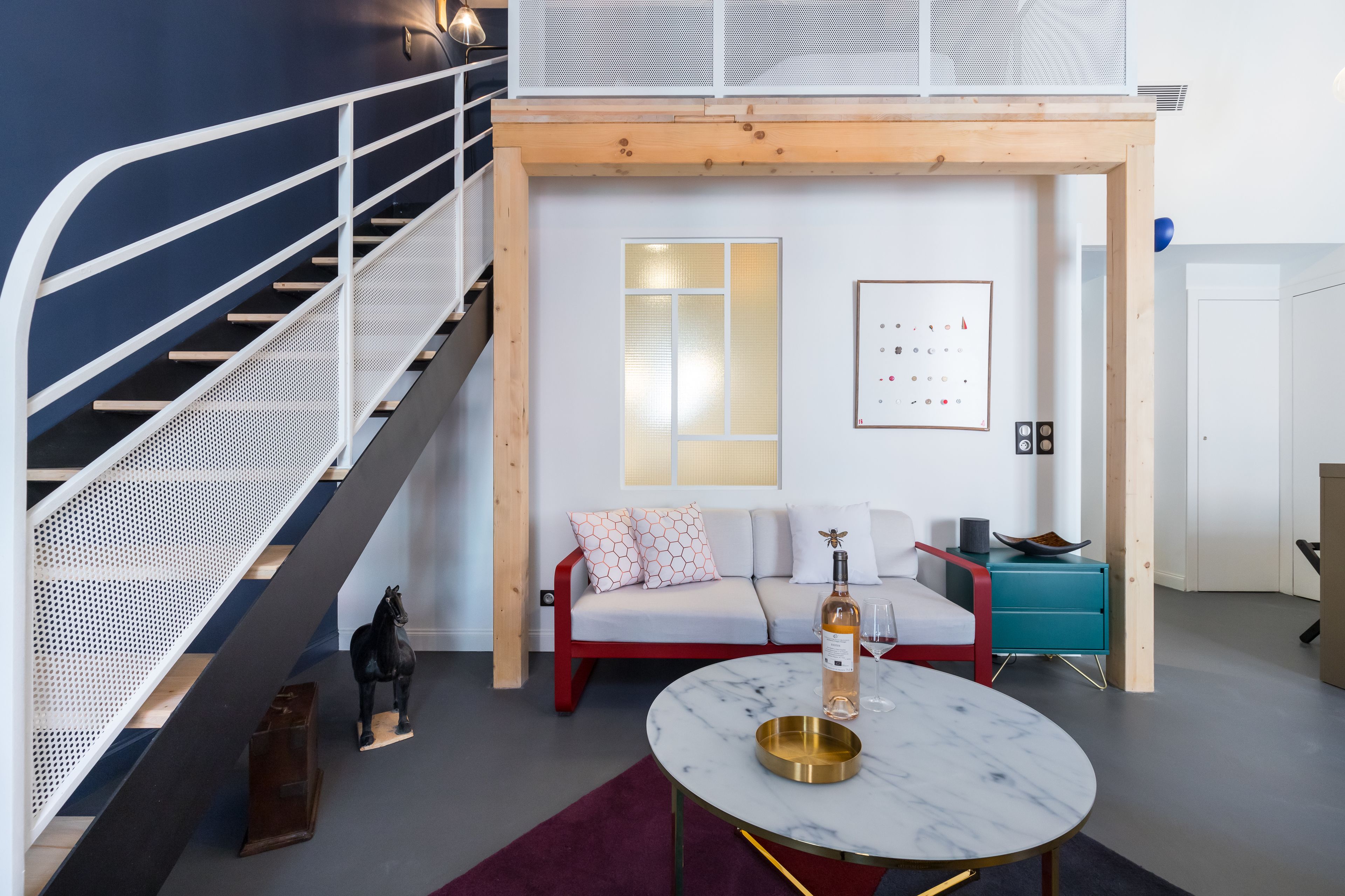 Een moderne leefruimte met een trap, een bank, een salontafel en een kunstwerk aan de wand.