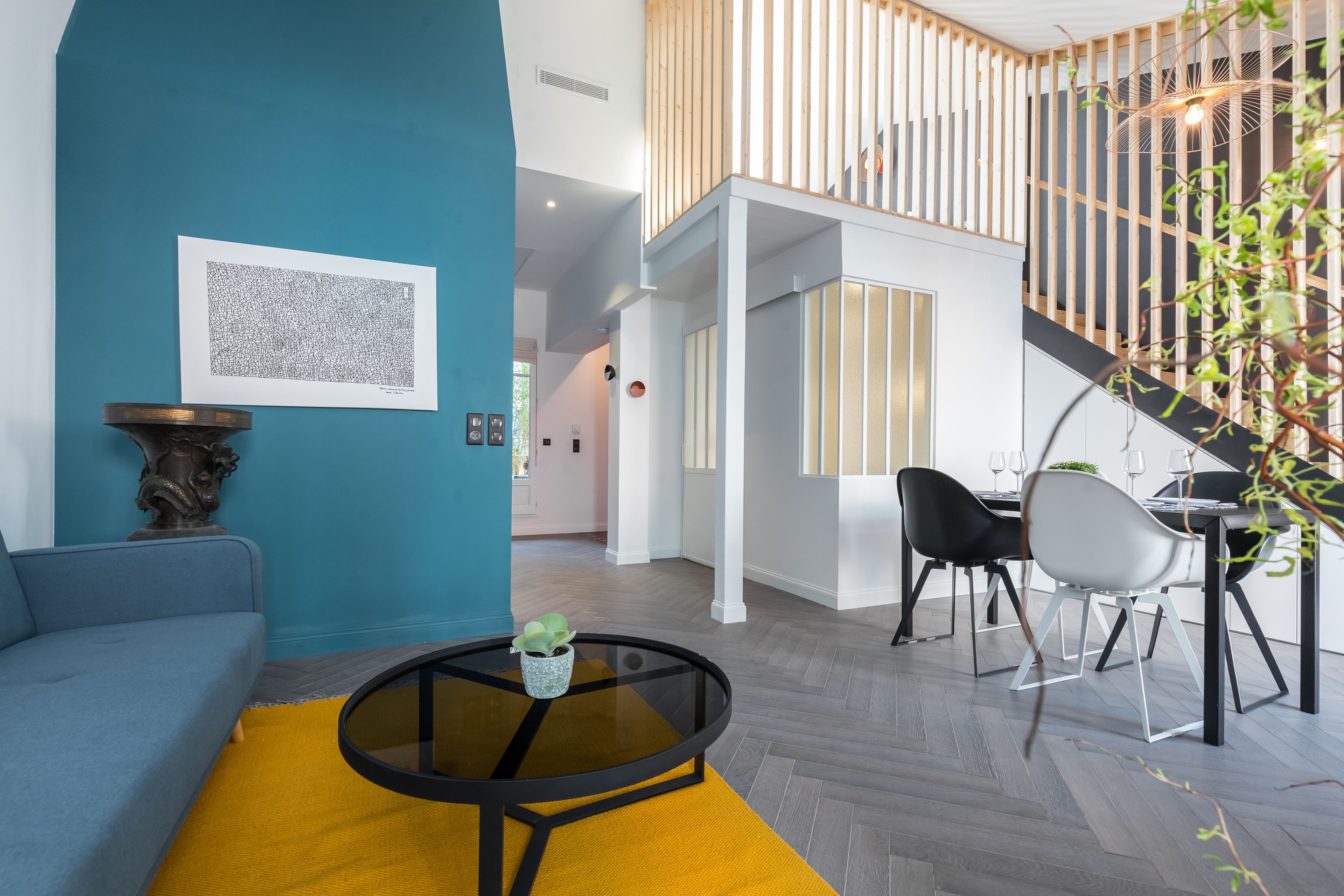 A modern living room with a blue wall, a round glass coffee table, a sofa, and a dining area with chairs and a table.