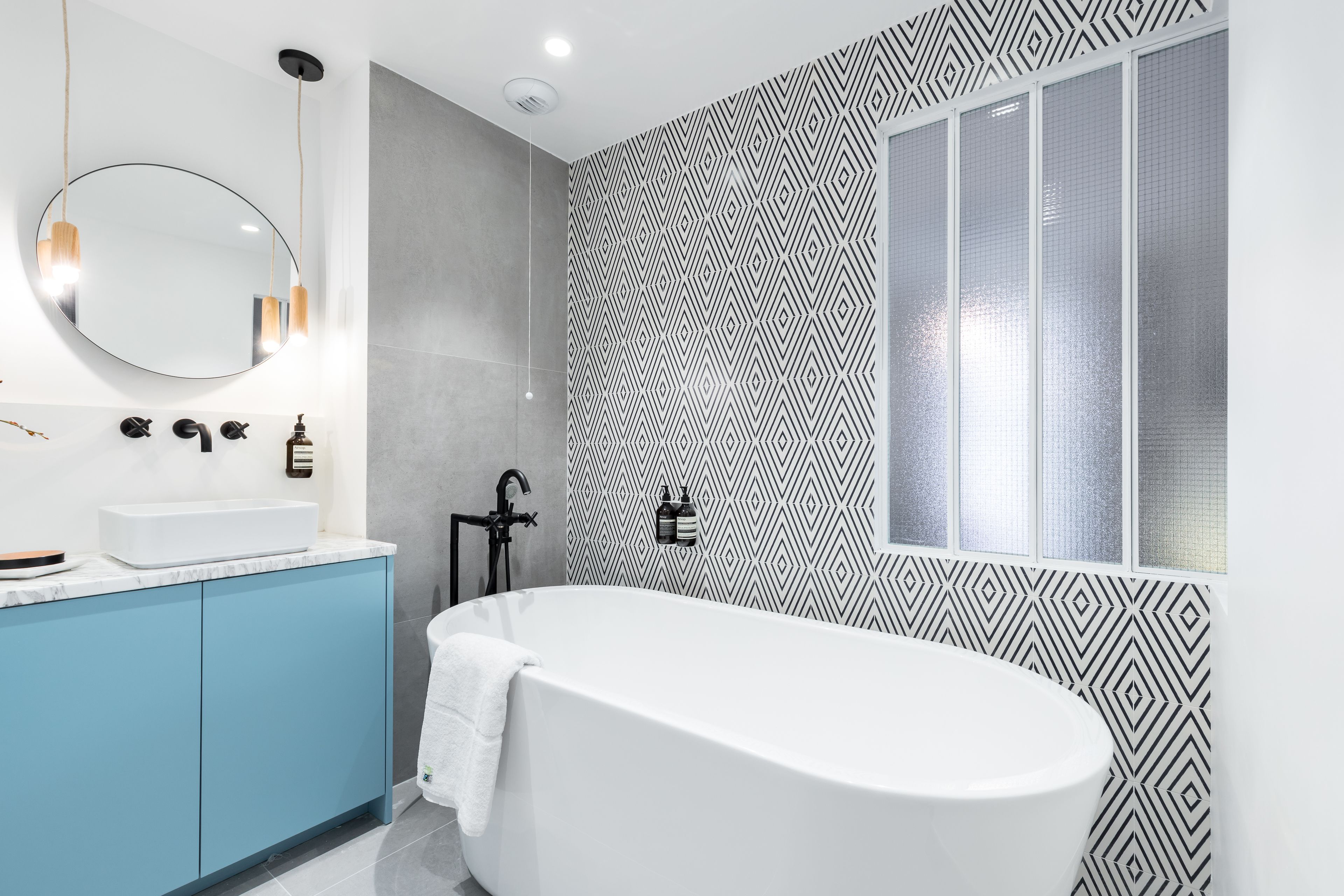 Un bagno moderno con una vasca freestanding, uno specchio rotondo e un muro decorato.