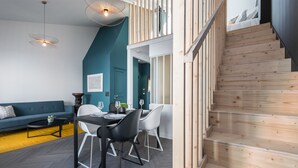 A modern living room with a dining area, a staircase, and a teal accent wall. - L'Abeille Boutique Apartments (Nice)