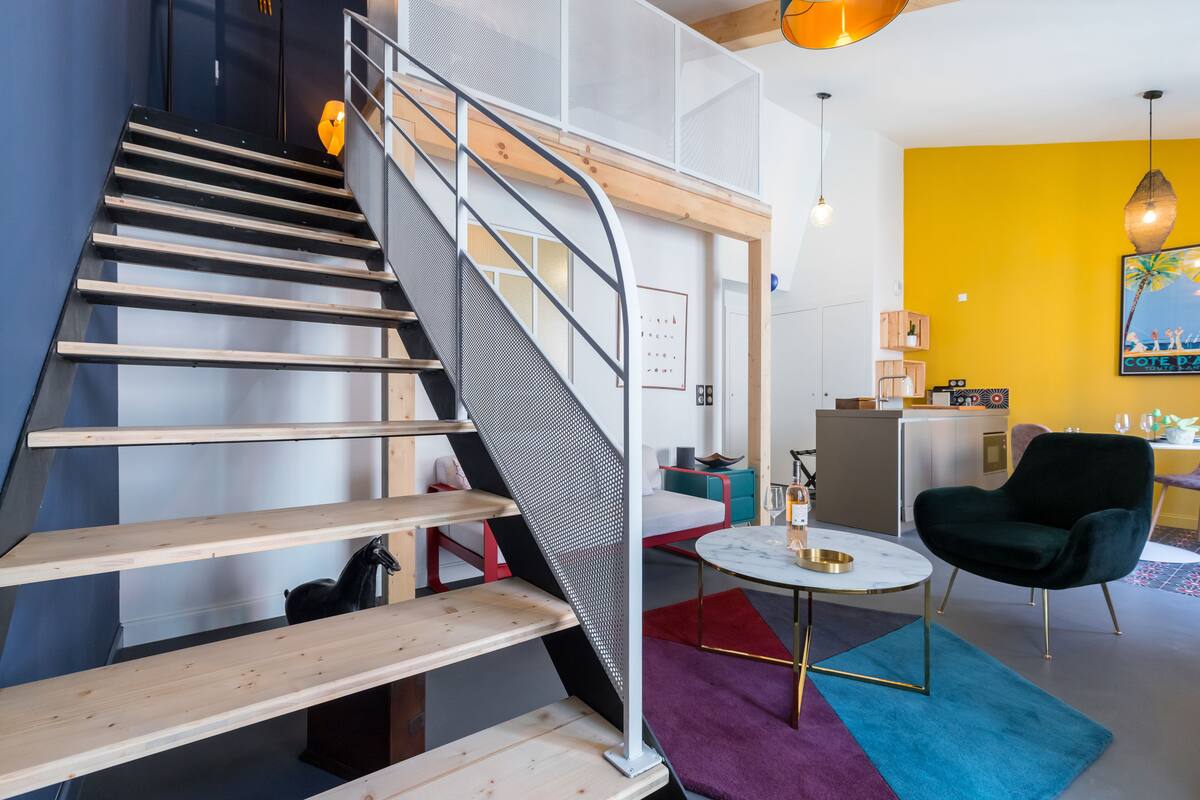 A modern interior with a wooden staircase, a black horse sculpture, a round table with a gold base, and a vibrant yellow wall.