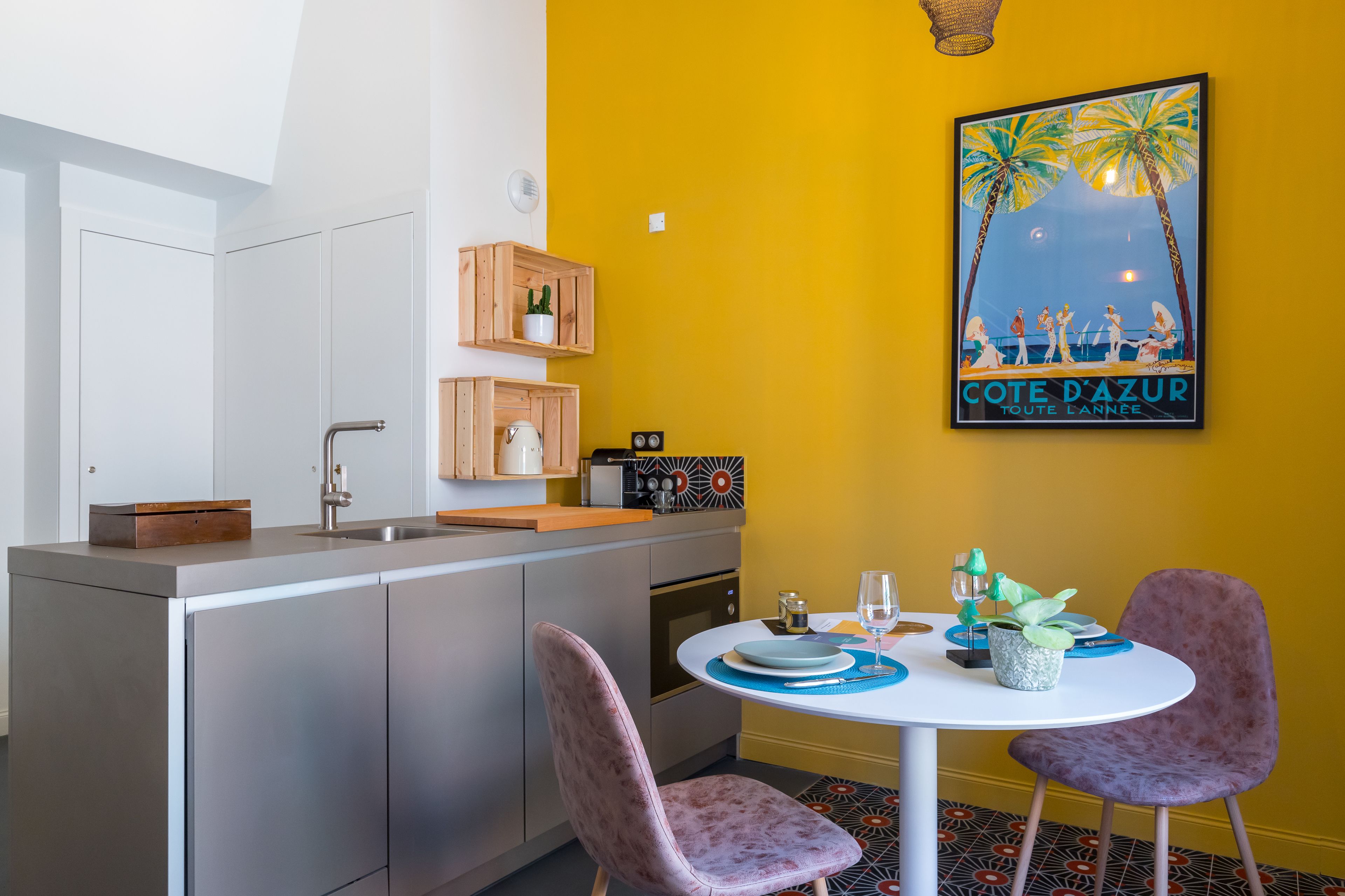 A compact kitchen with a central island, a dining area with two chairs, and a yellow wall with a poster.
