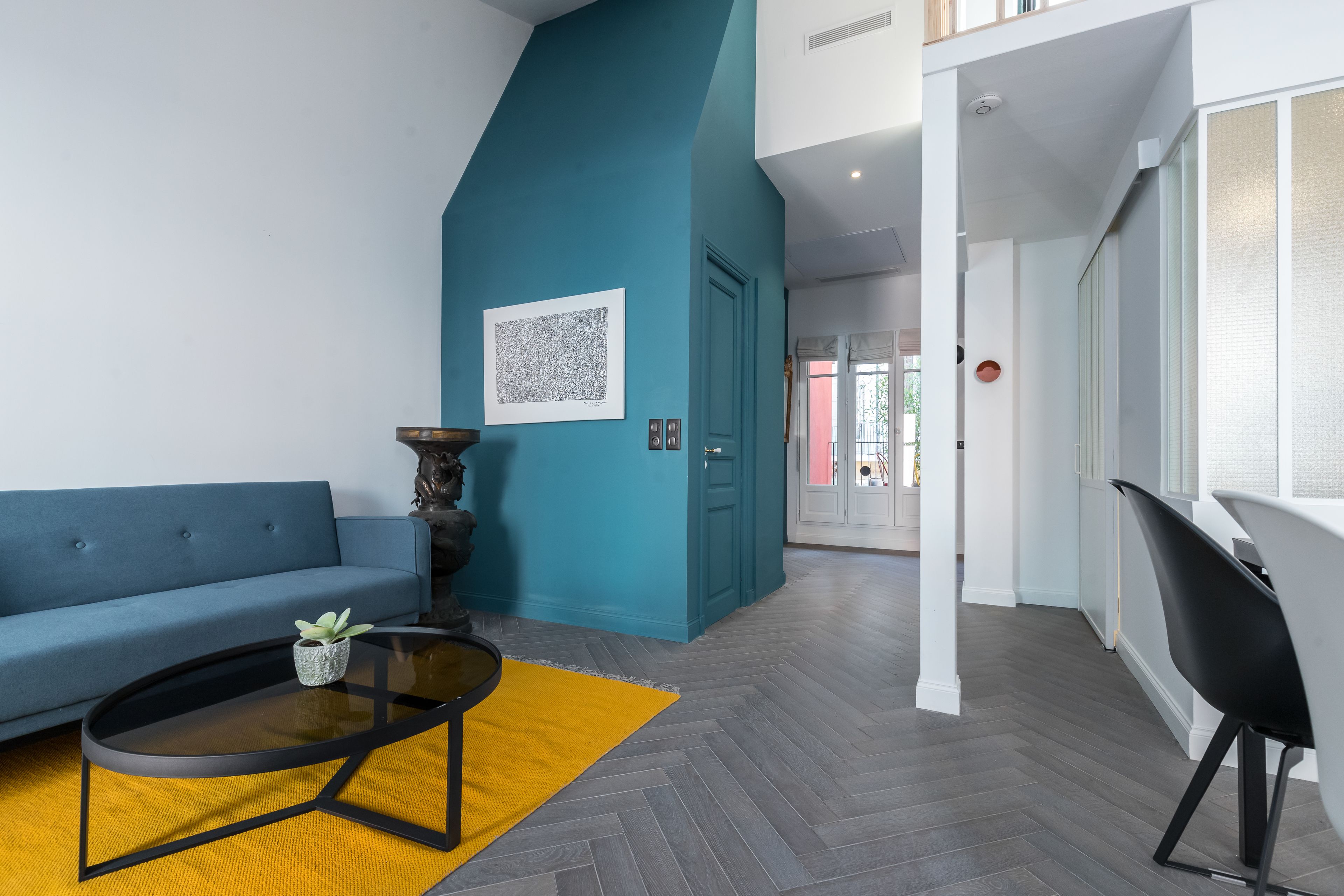 Un salon moderne avec un mur d’accent bleu, un canapé, une table basse et une vue sur une autre pièce.