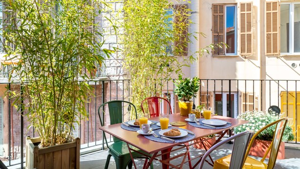 A balcony with a table set for breakfast, surrounded by potted plants and chairs. - L'Abeille Boutique Apartments (Nice)