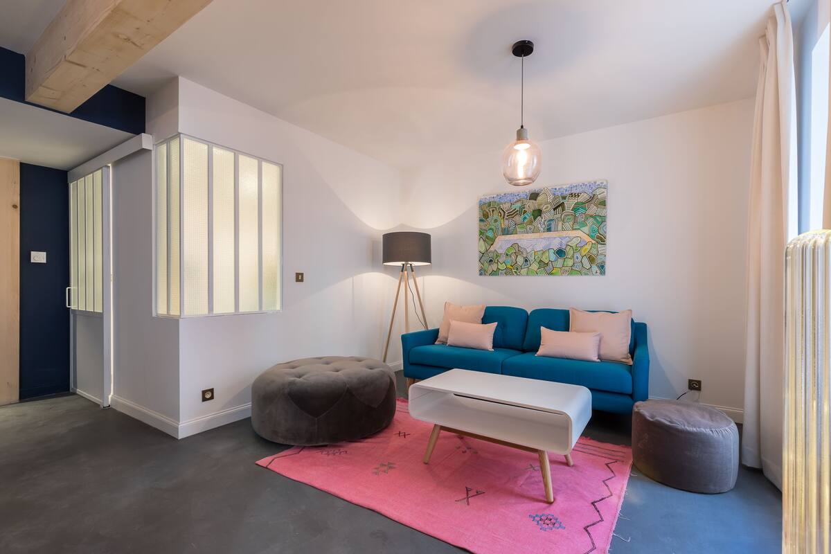 A modern living room with a blue sofa, a white coffee table, a grey ottoman, and a pink rug.