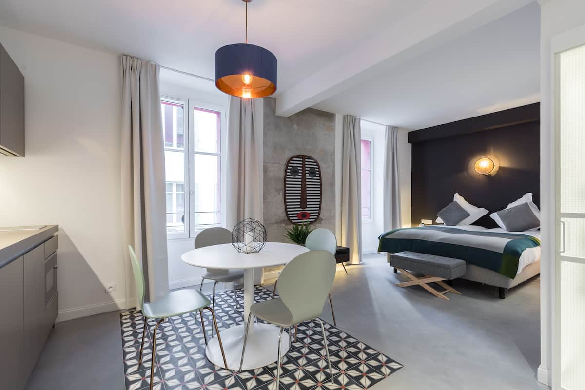 A modern hotel room with a dining area, a bed with a headboard, and a large window.