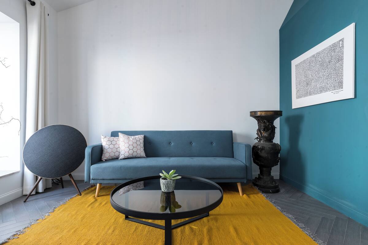 A modern living room with a blue sofa, a round coffee table with a plant, a large abstract painting, and a decorative floor lamp.