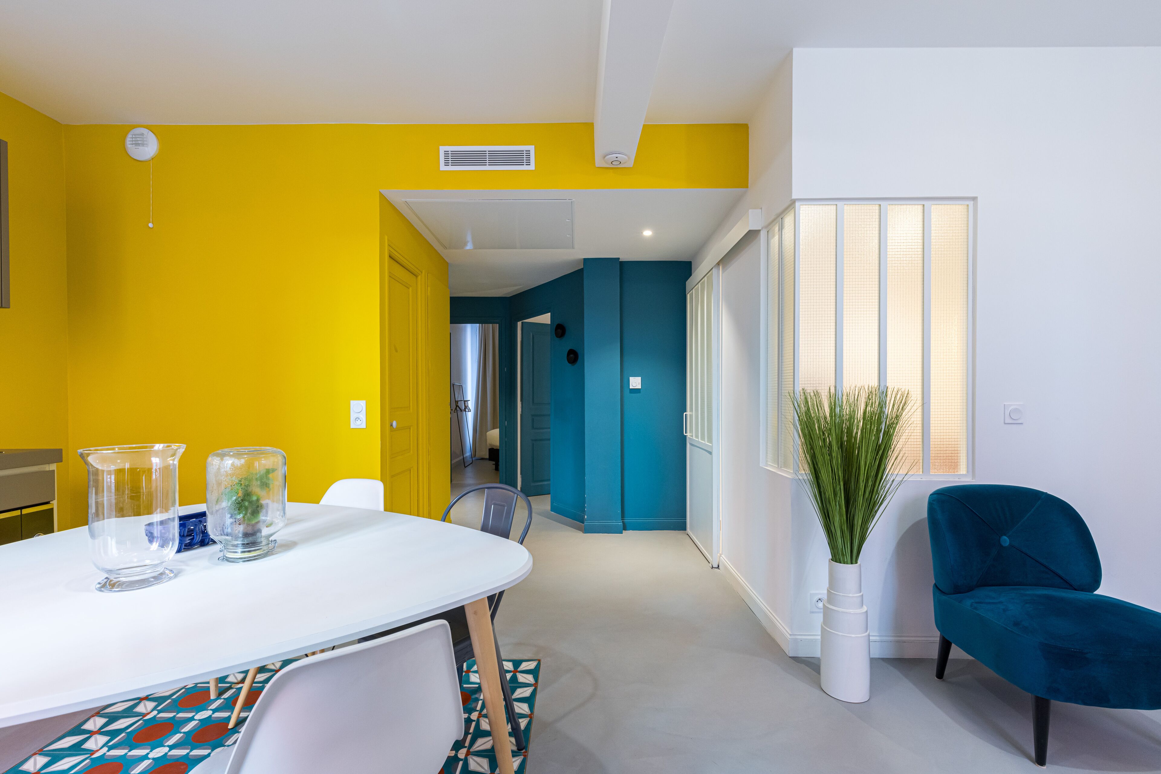 Una habitación moderna con una mesa blanca, una silla verde azulada y una planta en maceta.