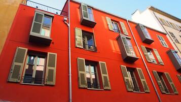 Un immeuble à plusieurs étages, doté de façades rouges et beiges, de nombreuses fenêtres avec volets et de balcons.