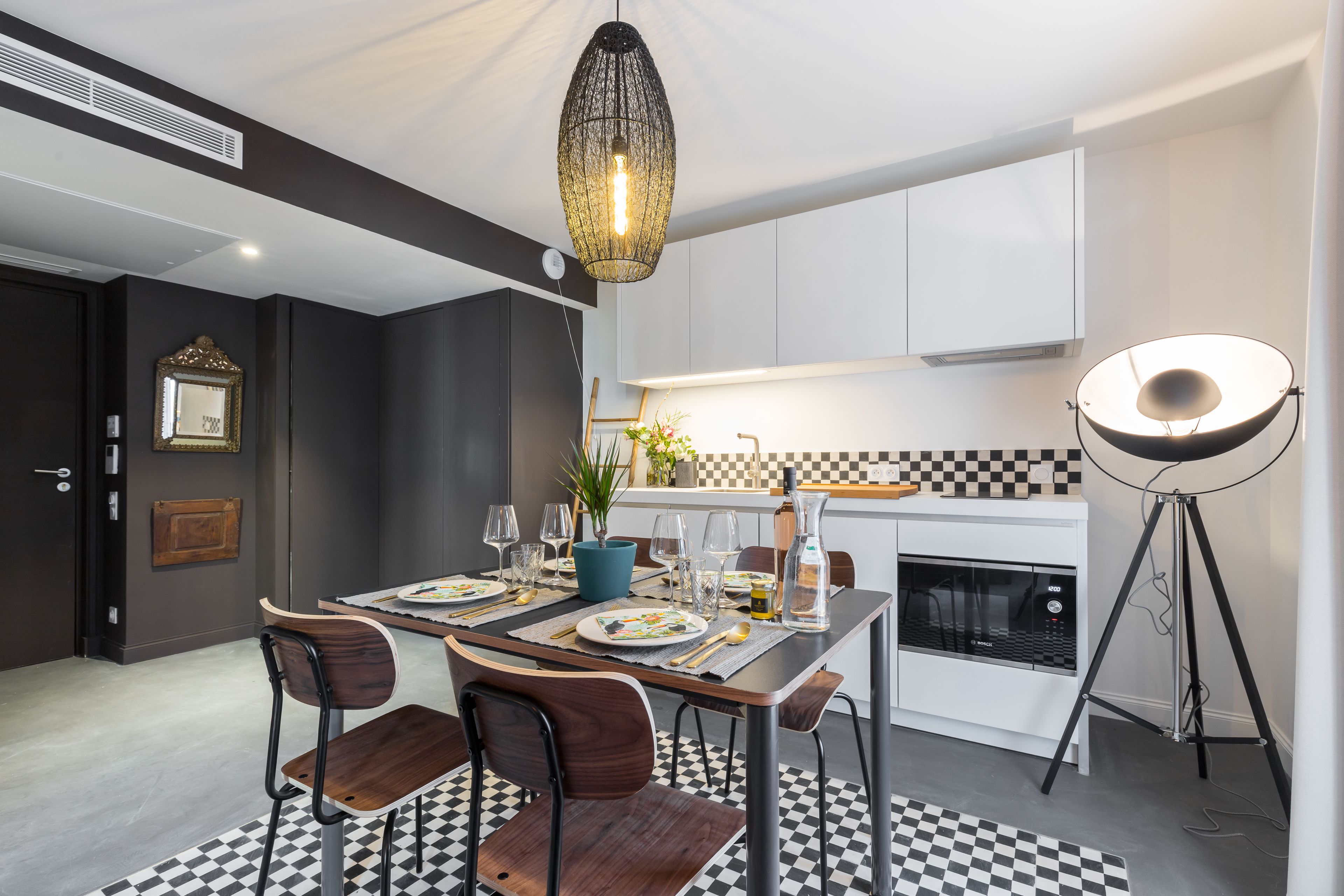 A modern kitchen with a dining table set for four, a pendant light, and a floor lamp.