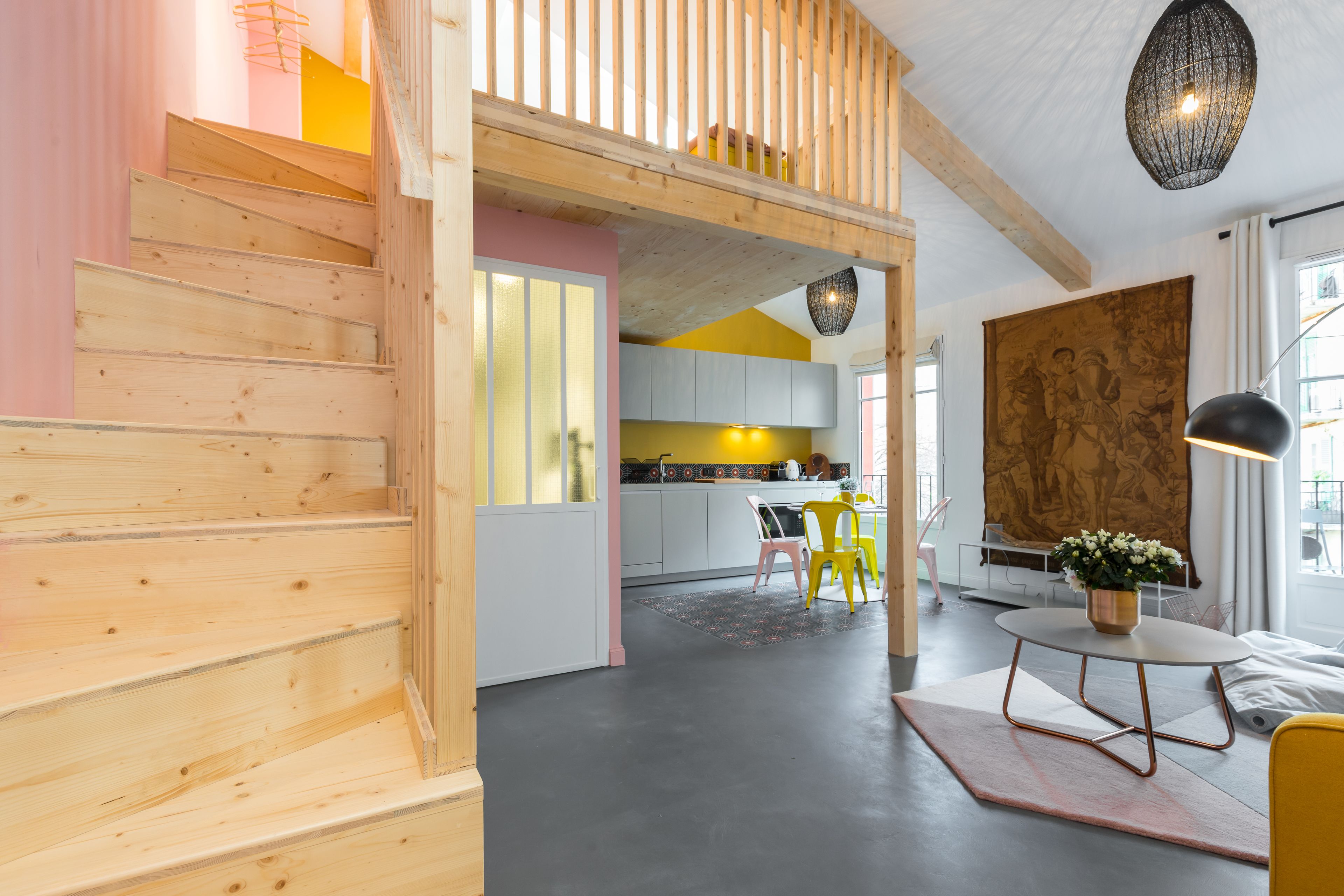 Un interior moderno con escaleras de madera, una zona de cocina y un espacio de comedor con sillas amarillas.