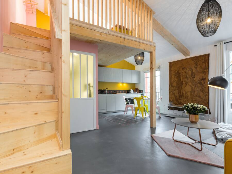 A modern interior with wooden stairs, a kitchen area, and a dining space with yellow chairs.