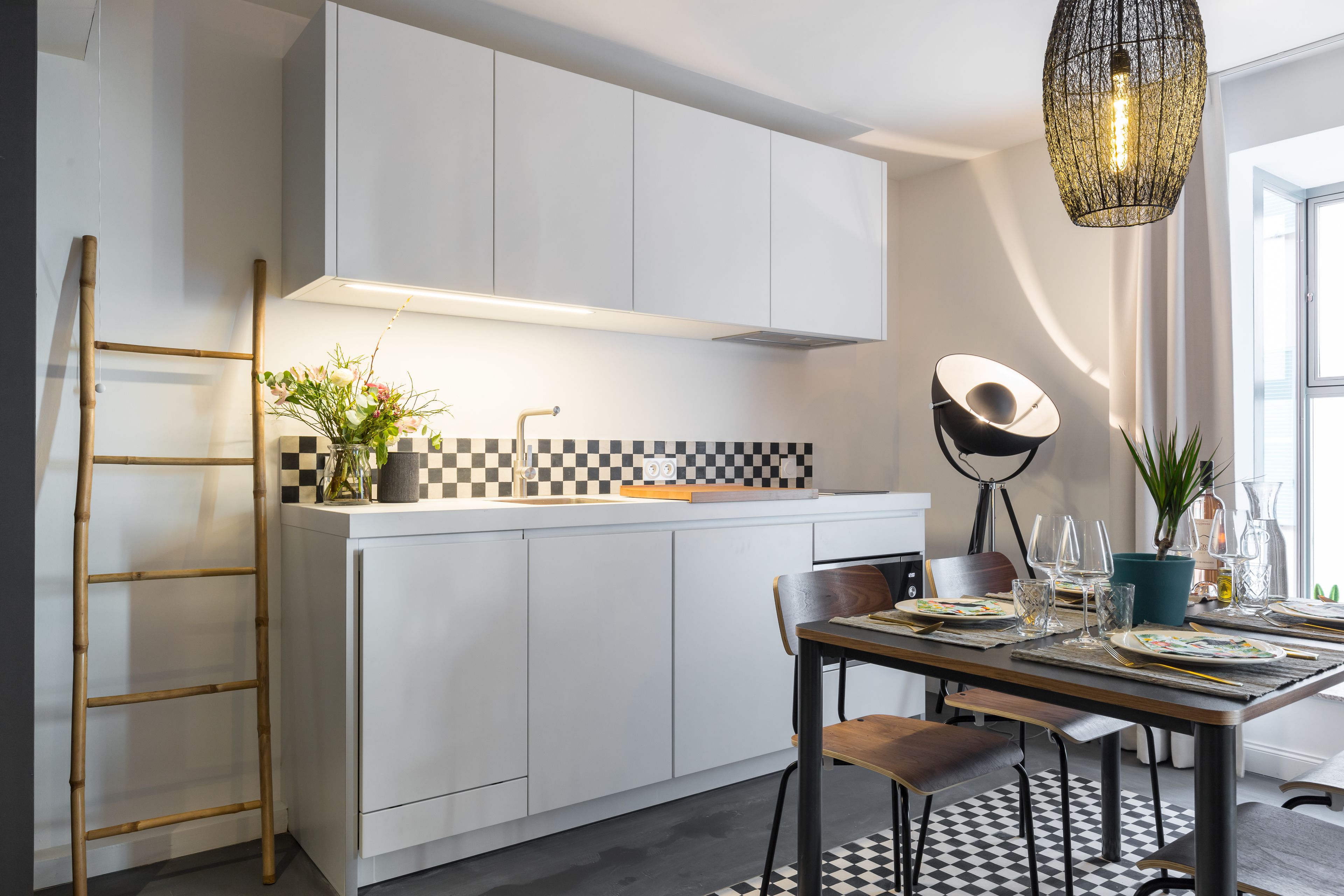 Une cuisine moderne avec des meubles blancs, un dosseret à carreaux et un coin repas avec une table dressée pour quatre personnes.