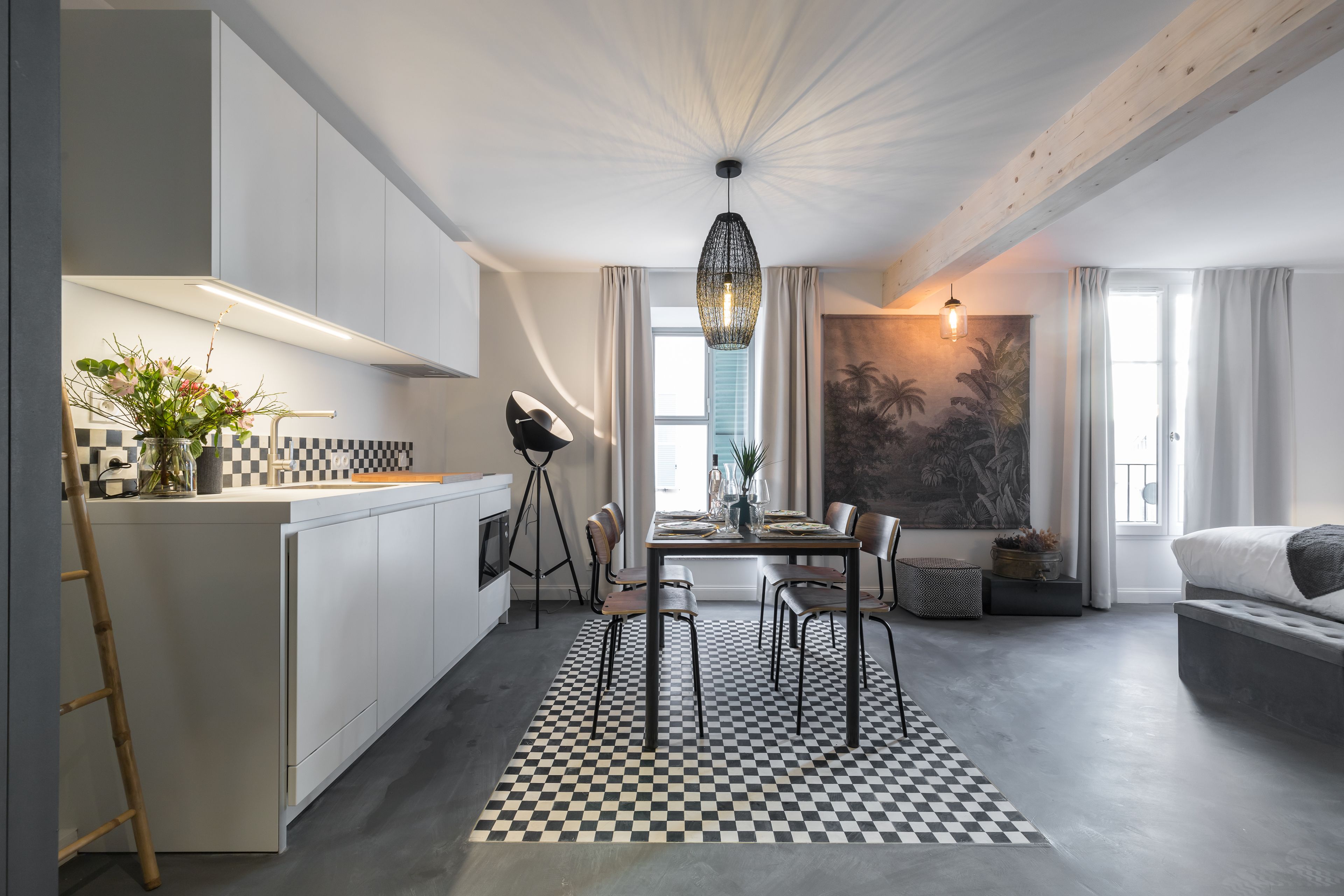 A modern kitchen with a checkered floor, a dining area with a table and chairs, and a living area with a sofa and a large window.