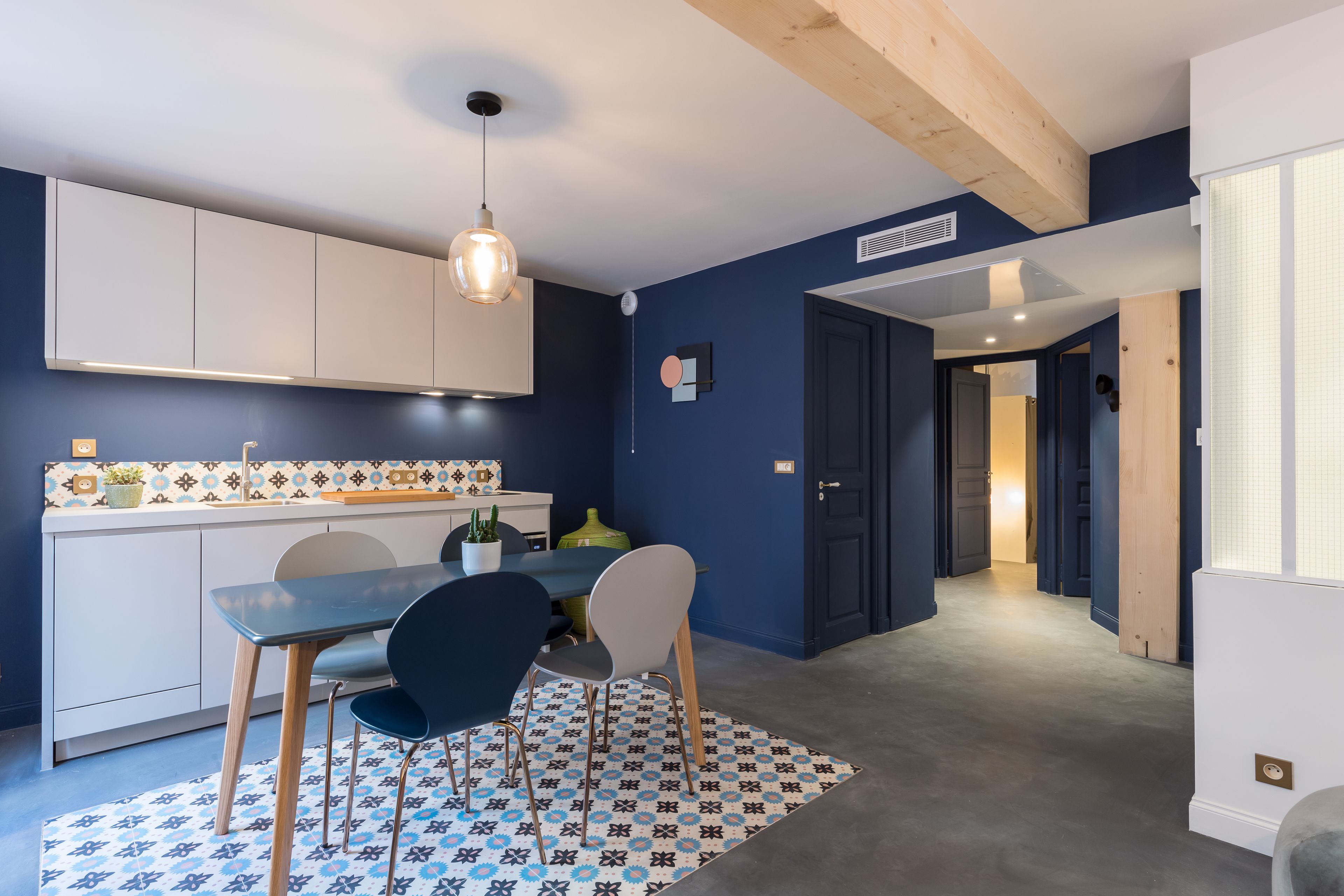 Una cocina moderna con armarios blancos, un comedor azul y una alfombra estampada.