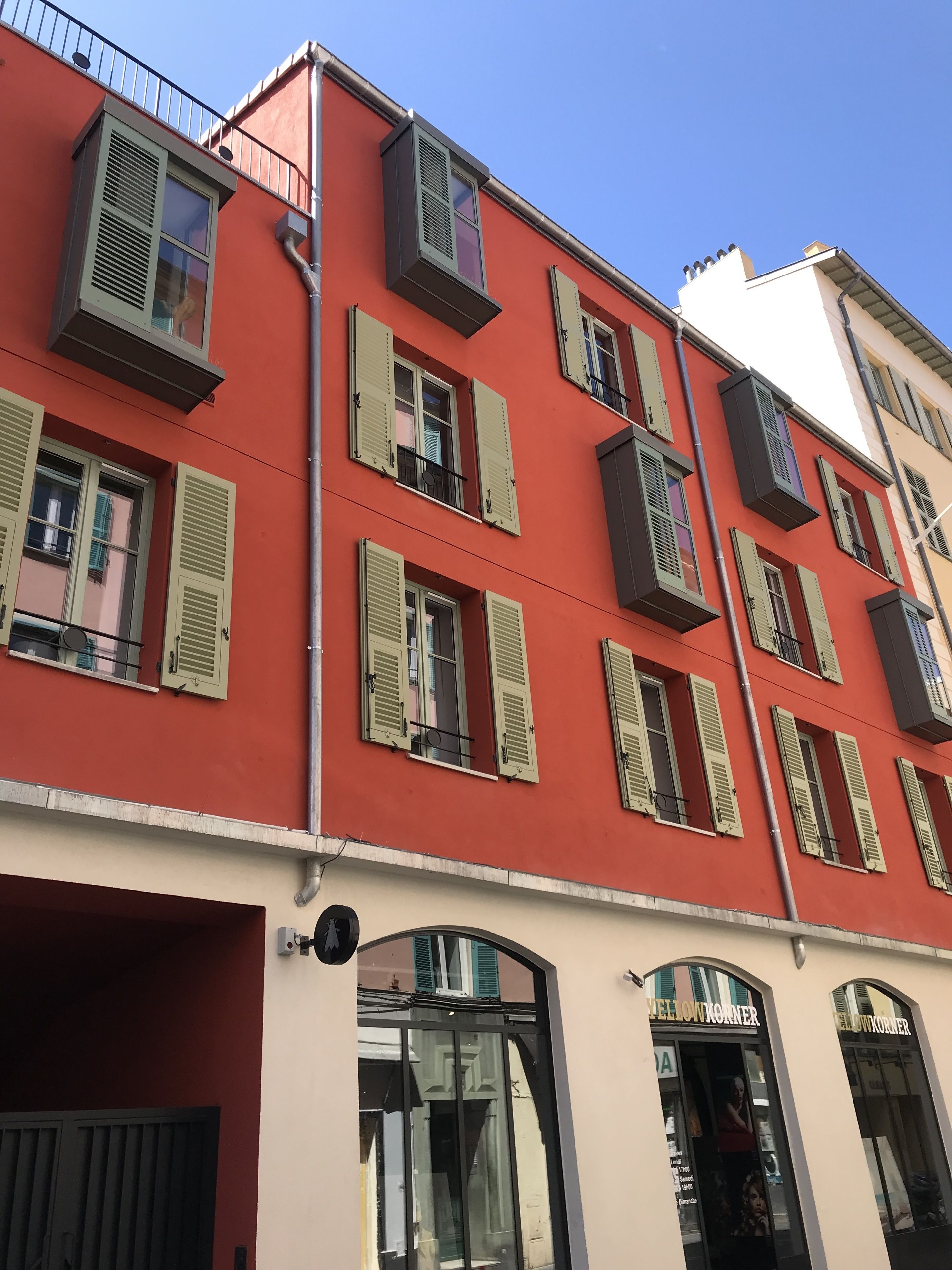 Un immeuble à plusieurs étages, aux façades rouges et blanches, doté de nombreux balcons et d'une devanture avec une enseigne.
