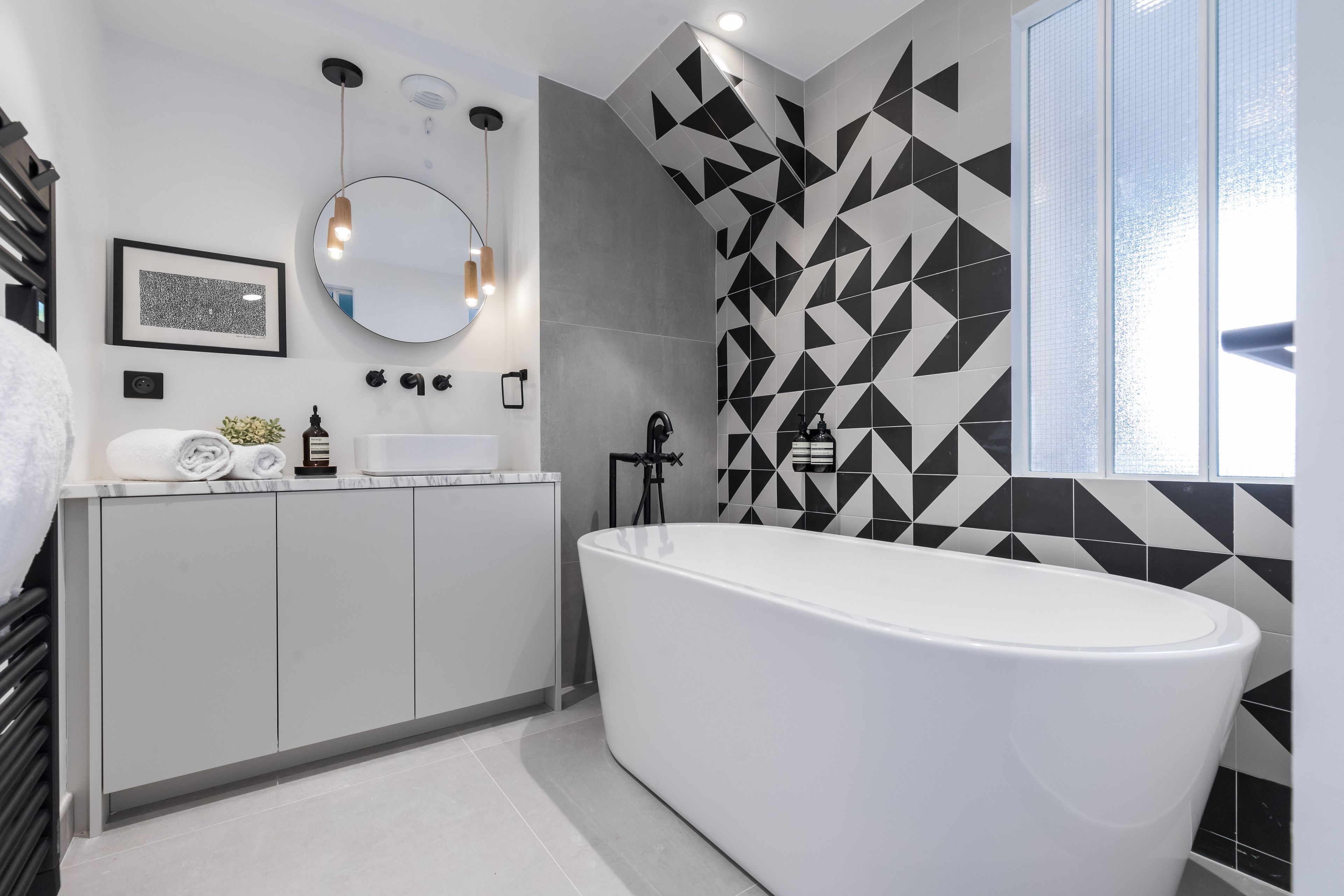 Une salle de bain moderne avec une baignoire sur pieds, un meuble-lavabo avec un miroir et des carreaux à motifs géométriques.