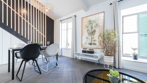 A modern dining area with a black and white chair set, a white bench, and a glass table with a plant. - L'Abeille Boutique Apartments (Nice)