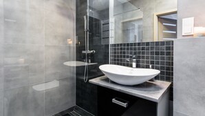 Ein modernes Badezimmer mit einem großen, weißen Waschbecken, einer Duschkabine aus Glas und einer gefliesten Spritzschutzwand.