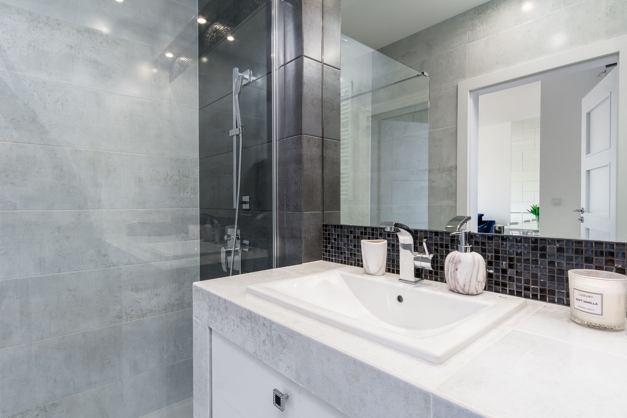 A modern bathroom with a large mirror, a glass-enclosed shower, and a white sink.
