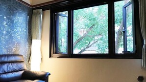 A room with a leather chair, a glass table, and a window with a view of trees. - Hotel Okus Kumamoto (Kumamoto)