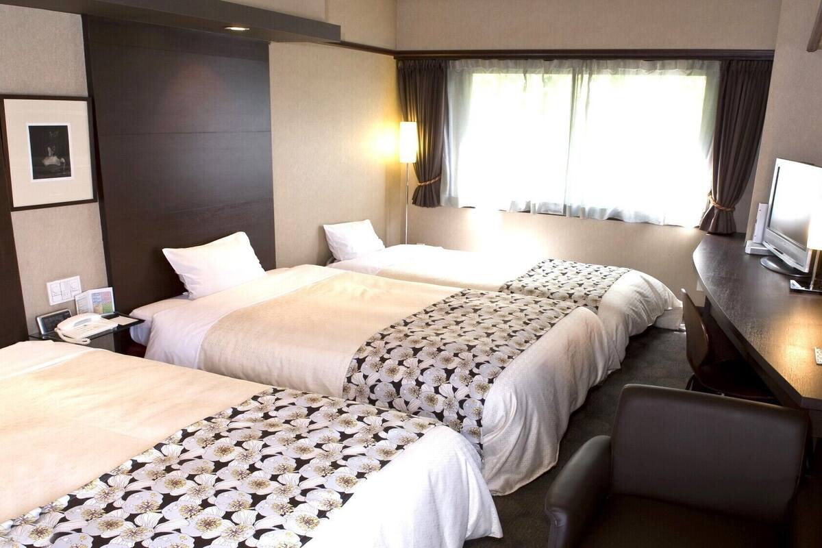 Ett hotellrum med två sängar, ett skrivbord med en dator, en stol och ett fönster med gardiner.