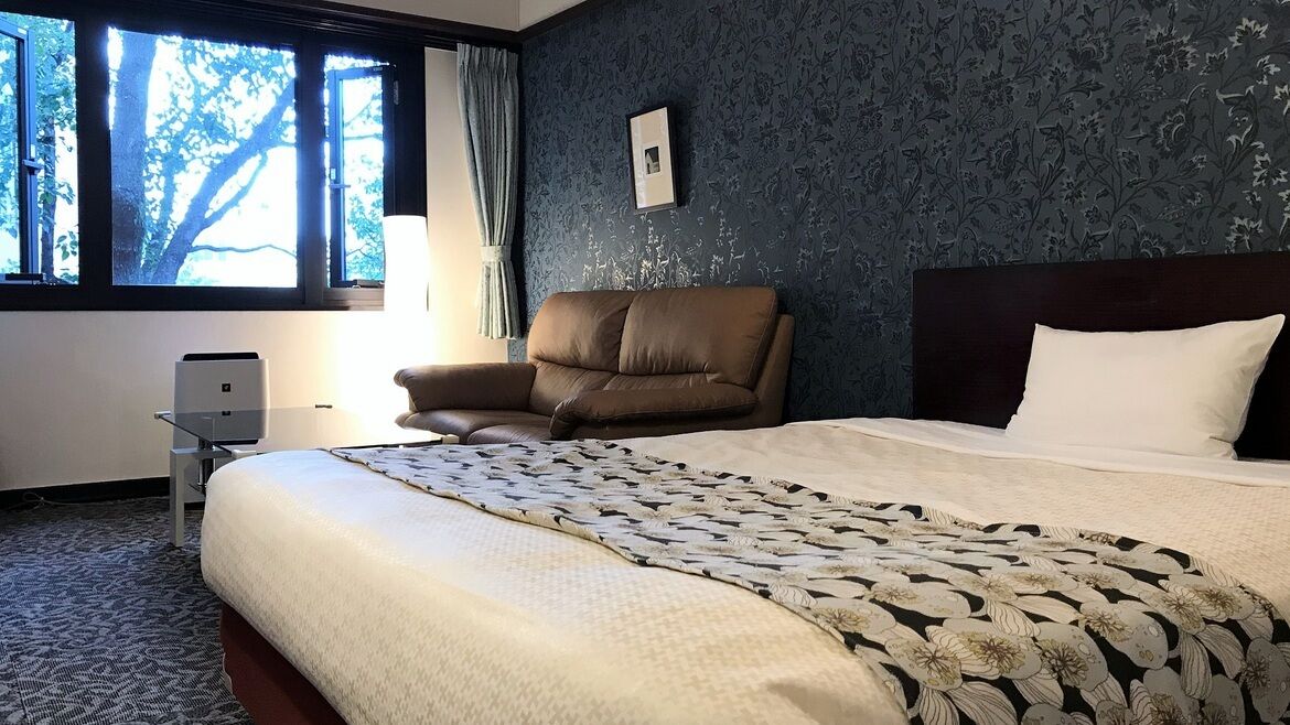 A hotel room with a large bed, a chair, a desk with a printer, and a window with curtains.