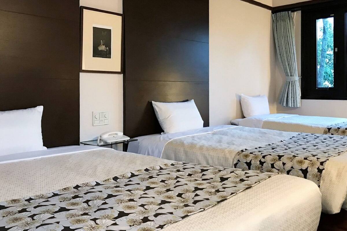 Ett hotellrum med två sängar, ett nattduksbord, en telefon och ett fönster med utsikt över träd.