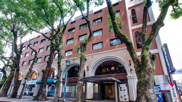 A hotel with a brick facade, large windows, and a prominent entrance with an archway. - Hotel Okus Kumamoto (Kumamoto)