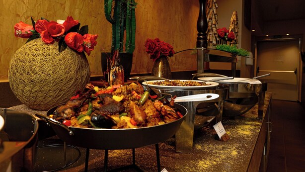 Een buffet met diverse gerechten, een decoratieve vaas met rode bloemen en een cactussplant.