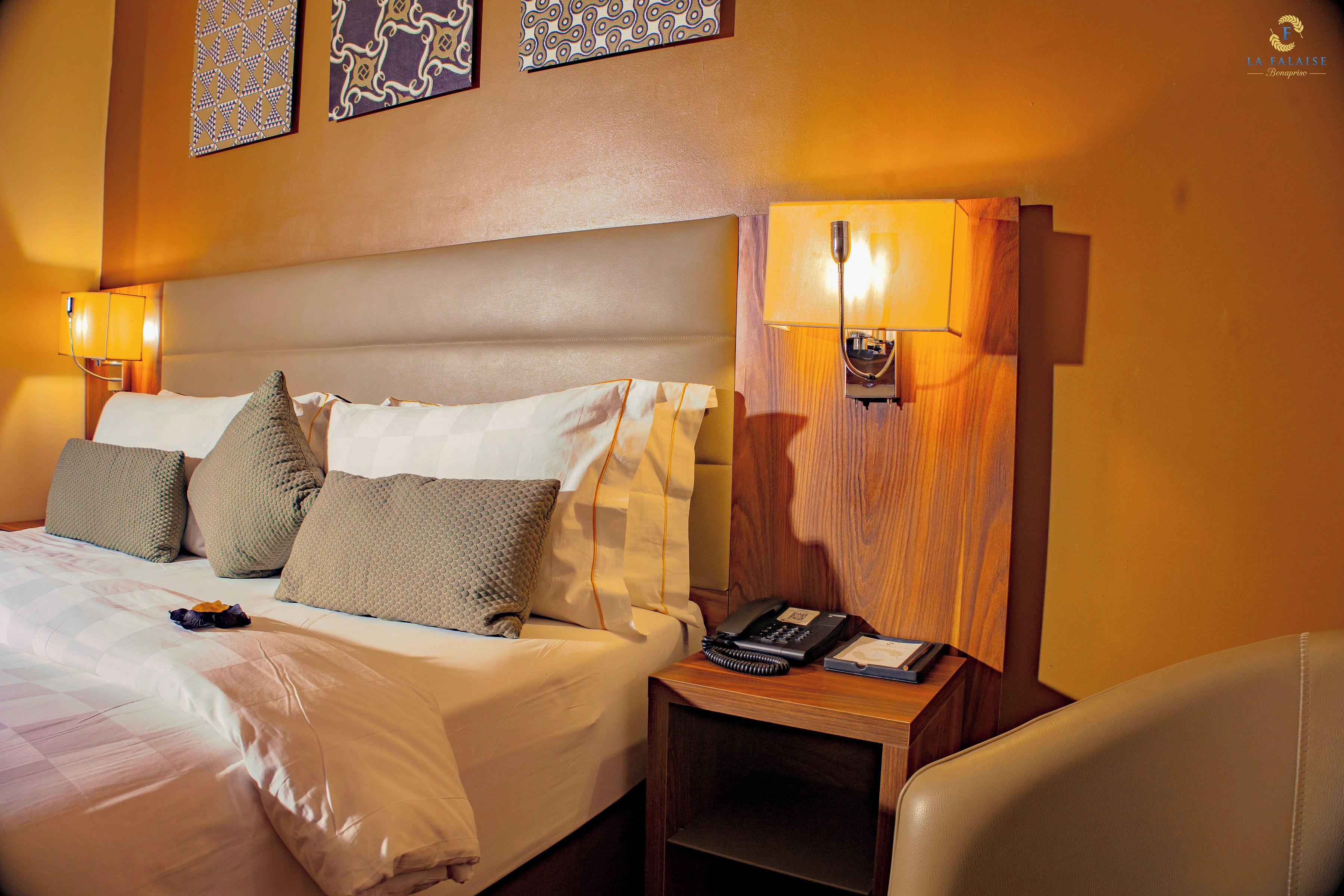 A hotel room with a bed, pillows, a bedside table with a telephone, and wall-mounted lamps.