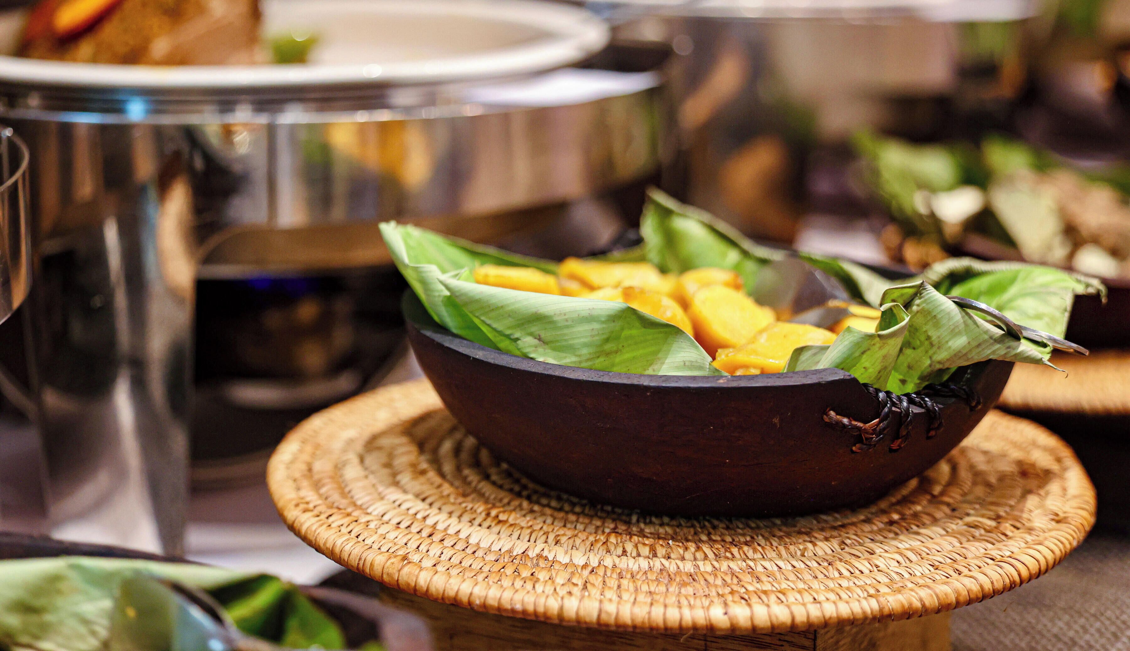 A bowl of food with banana leaves on a woven mat.