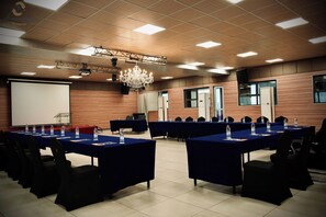 A conference room with tables, chairs, a projector screen, and a chandelier. - Hotel La Falaise Bonapriso (Douala)