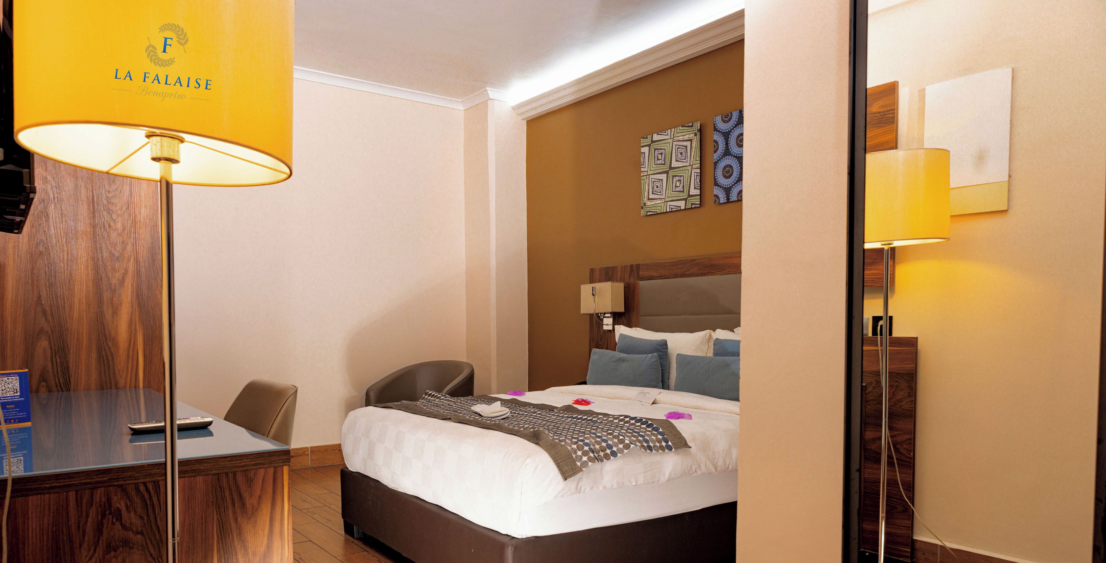 A hotel room with a bed, bedside table, chair, desk, and a lamp.