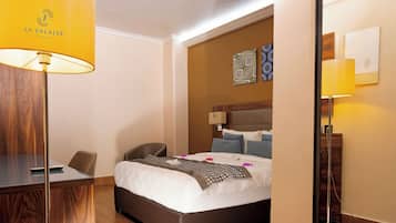 A hotel room with a bed, bedside table, chair, desk, and a lamp.