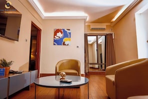 A hotel room with a round table, two chairs, a potted plant, a painting on the wall, and a door leading to another room. - Hotel La Falaise Bonapriso (Douala)