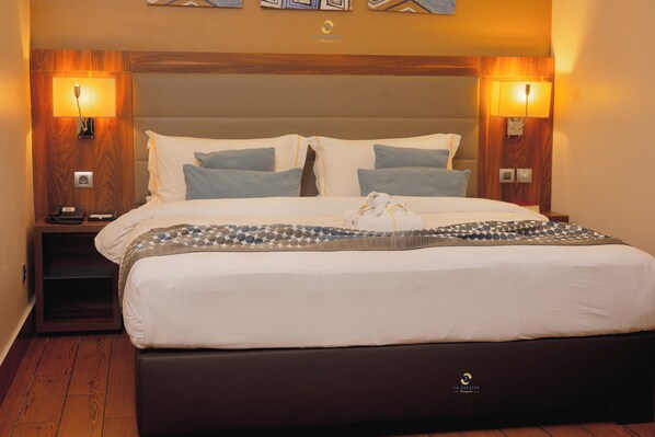 A hotel room with a large bed, two bedside tables, and wall-mounted lamps. - Hotel La Falaise Bonapriso (Douala)