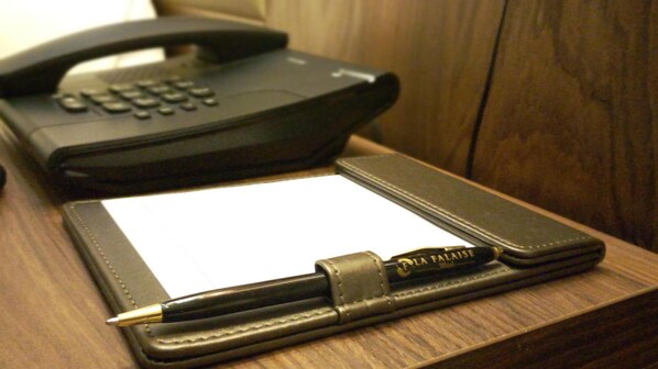 Un teléfono negro, una libreta blanca y una pluma sobre una superficie de madera.